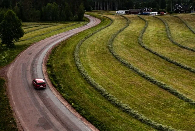 Bil på slingrande väg intill slåtterfält sedd från ovan