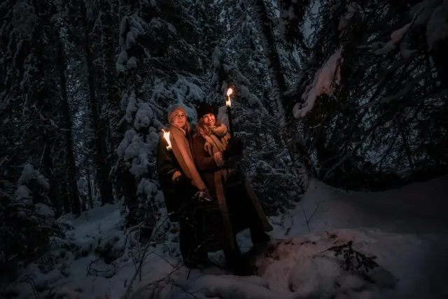 Två personer med facklor i snötyngd skog i mörker