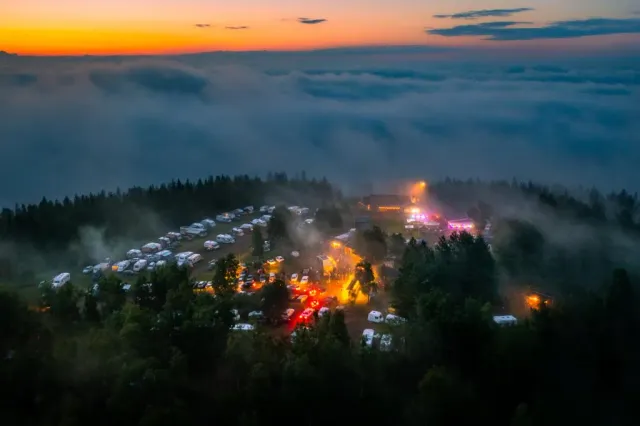Campingområde med ljus och dimma i skogen vid solnedgång sett från ovan