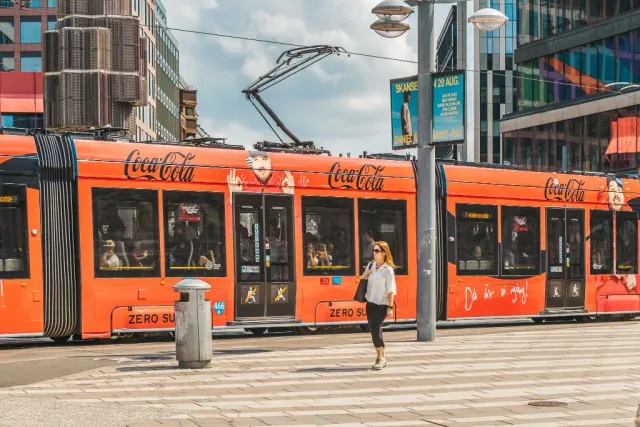 Orange spårvagn på en stadsgata med person som går över övergångsställe