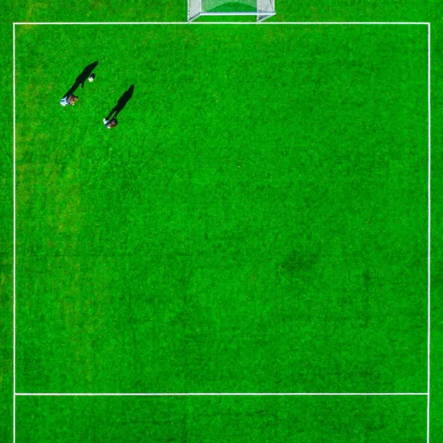 Två personer på en grön fotbollsplan sedd rakt uppifrån