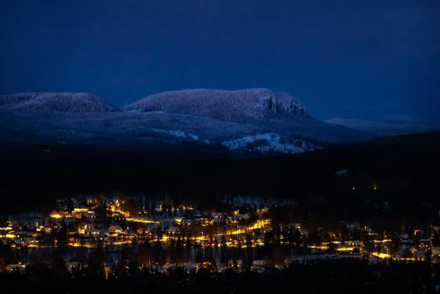 Upplyst by i dal under snöklädda fjäll i blå skymning