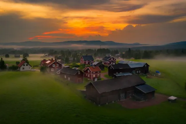 Röda hus i by med dimma och orange solnedgång sedd från ovan