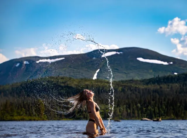 Kvinna kastar hår och vattenstänk framför fjäll och sjö