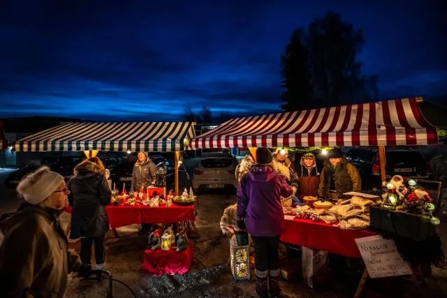 Julmarknad med röd-vitrandiga tält och besökare i skymning