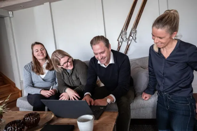 Fyra personer skrattar framför en bärbar dator i en soffa
