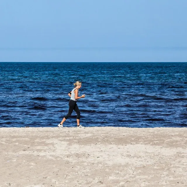 Kvinna joggar längs en sandstrand vid blått hav
