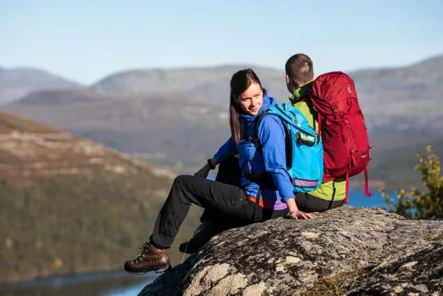 Två vandrare med ryggsäckar sitter på en klippa med utsikt över fjäll