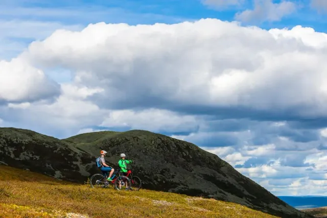 Två mountainbikecyklister på en fjällsluttning under stora moln
