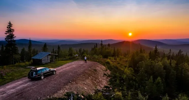 Bil och stuga vid grusväg på fjäll i solnedgång