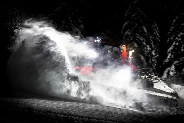Pistmaskin virvlar upp snö i mörkret