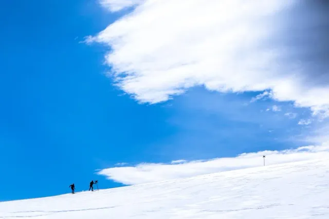 Två skidåkare på snöfjäll under blå himmel och moln