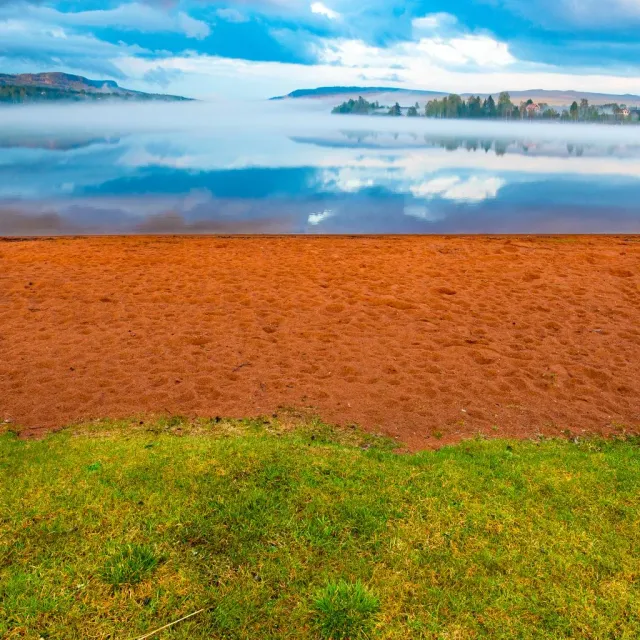 Sandstrand och gräs framför dimmig sjö och moln