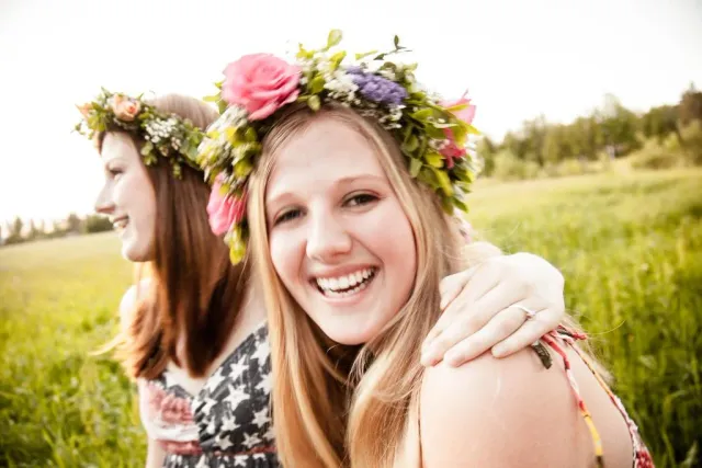 Två skrattande unga personer med blomsterkransar på en äng