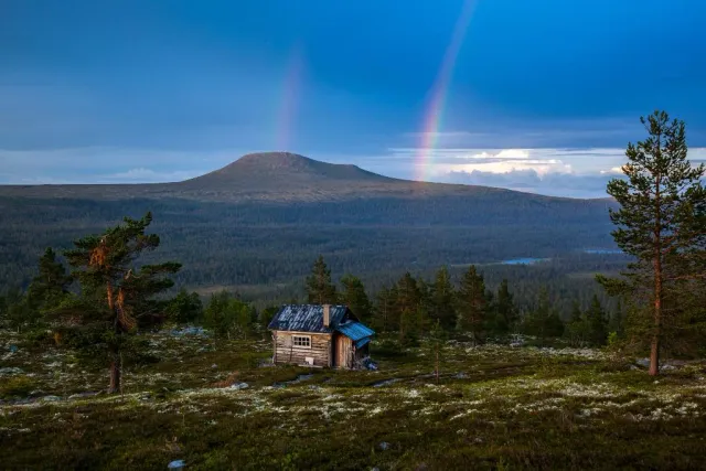 Stuga på fjällhed med fjäll och regnbåge i bakgrunden