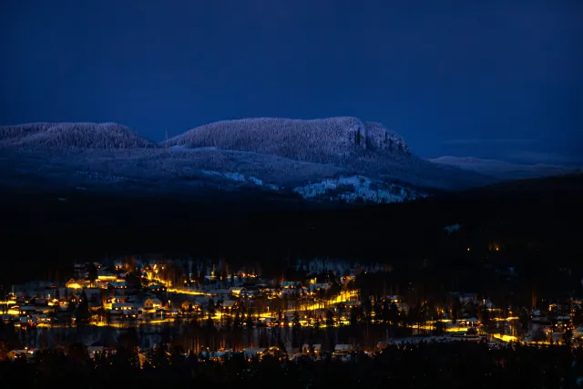 Upplyst by i dal under snöklädda fjäll i blå skymning