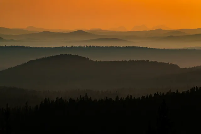 Skogsklädda åsar i orange dimma vid solnedgång