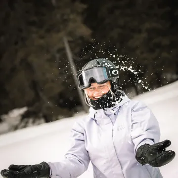 Skrattande person med skidhjälm och goggles får snö i ansiktet