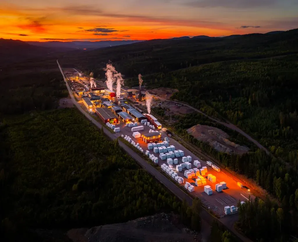 Upplyst industriområde i skogen vid solnedgång sett från ovan