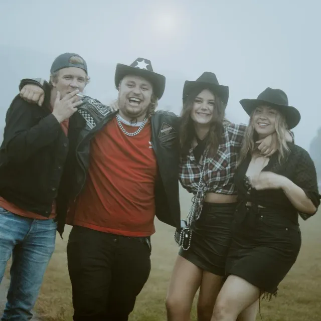 Fyra personer i cowboyhattar kramas utomhus
