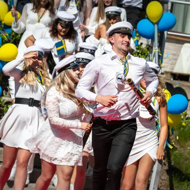 Studenter i vita mössor och klänningar går med ballonger