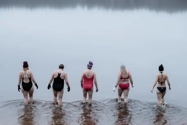 Fem personer i badkläder vadar ut i en dimmig sjö