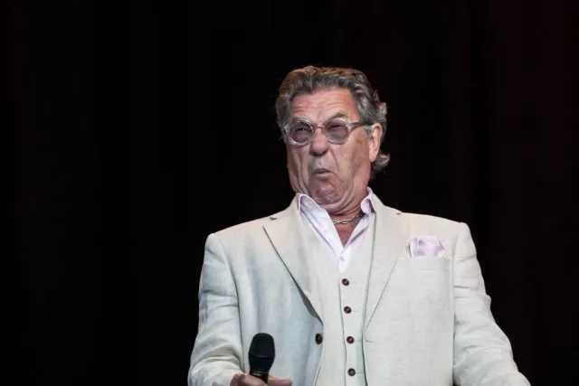 Man i ljus kavaj med mikrofon gör en min