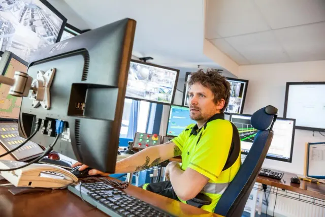 Man i varselkläder sitter vid skärmar i ett kontrollrum