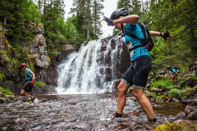 Cyklister korsar en å vid ett vattenfall i skogen