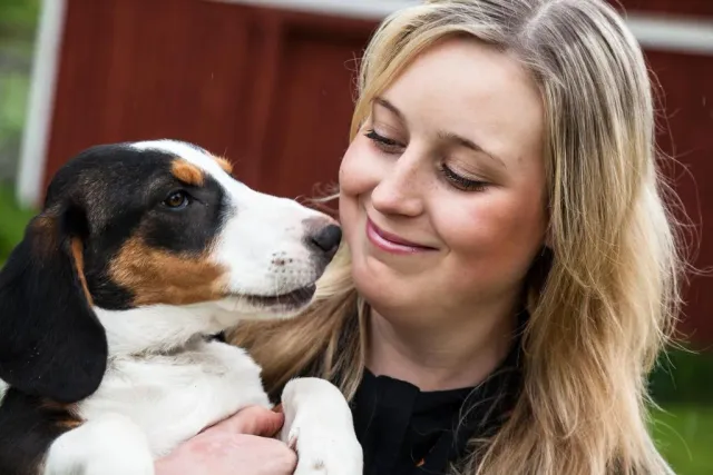 Leende kvinna kramar en hund som nuddar hennes kind