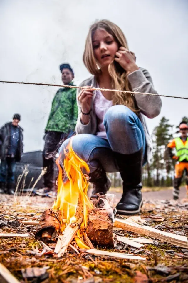 Ung kvinna hukar vid en liten brasa utomhus