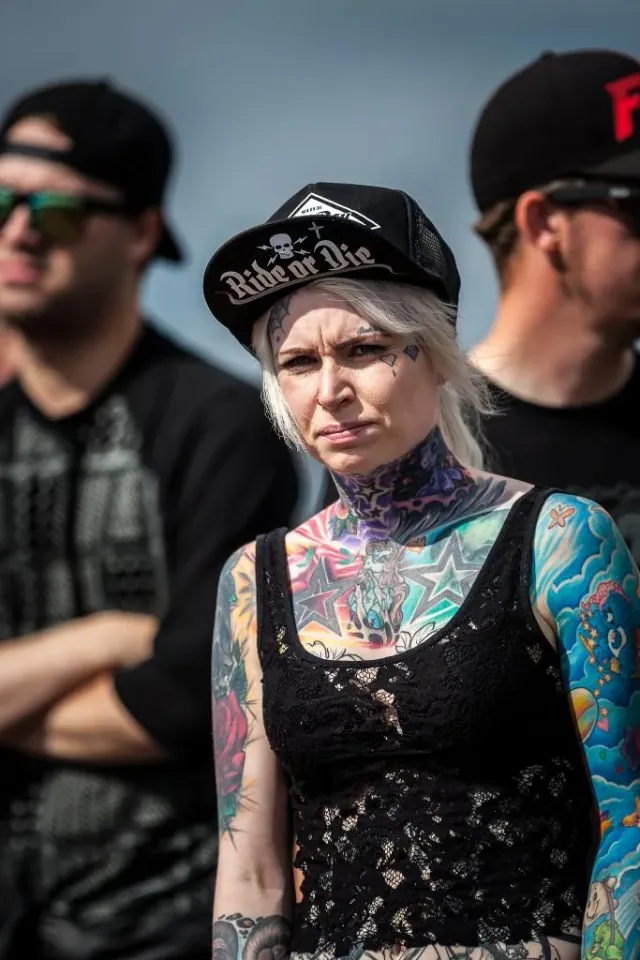 Kvinna med keps och tatuerad hals står bland människor