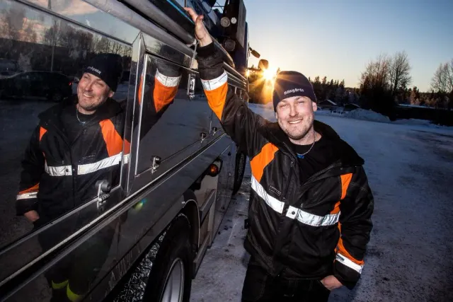 Två män i arbetskläder skrattar vid en buss