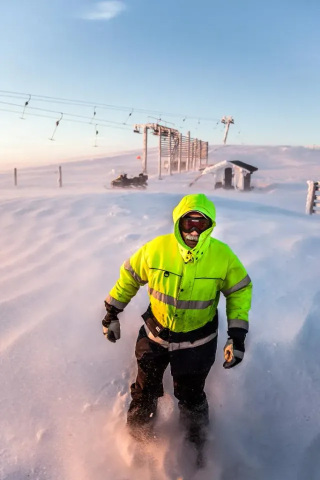 Person i gul varseljacka går i djup snö vid en skidlift