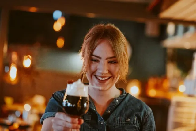 Leende kvinna håller upp ett glas på en bar