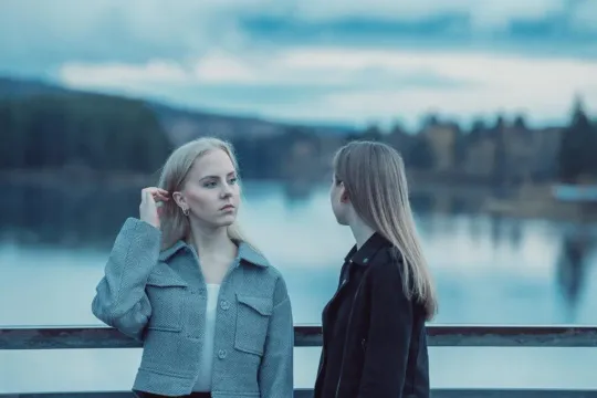 Två unga kvinnor står vid ett räcke framför en sjö