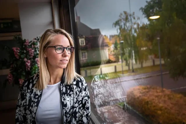 Kvinna med glasögon blickar ut genom ett fönster