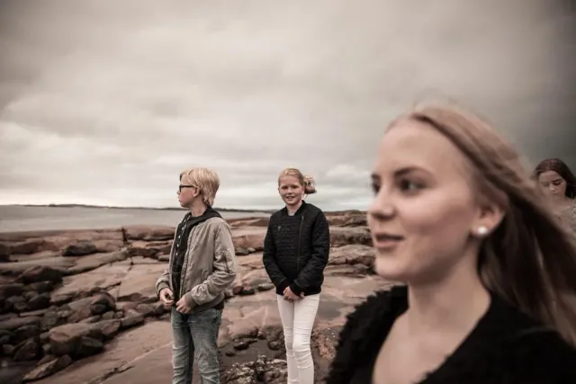 Tre unga personer står på klippor vid havet