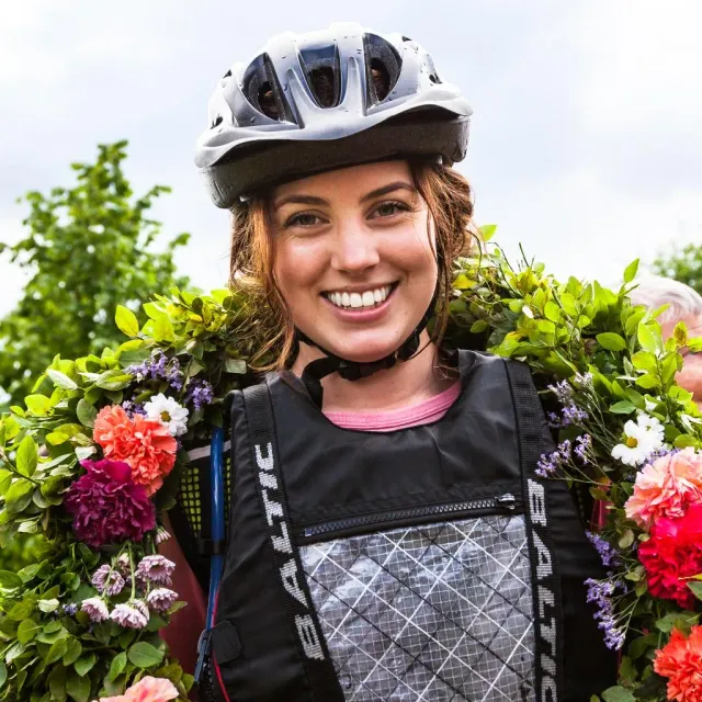 Leende kvinna med cykelhjälm och blomsterkrans runt halsen