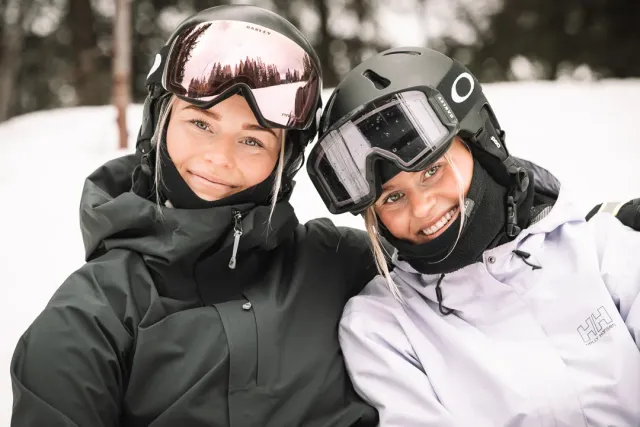 Två personer i skidhjälmar och goggles lutar sig mot varandra