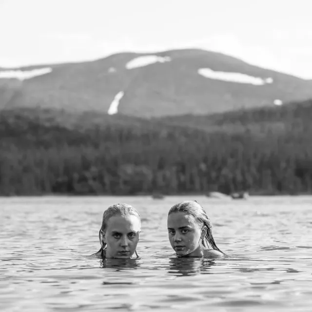 Två personer i vattnet framför fjäll i svartvitt