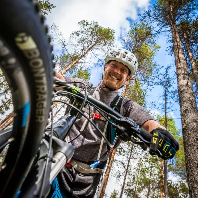 Leende mountainbikecyklist med hjälm sedd nerifrån bland tallar