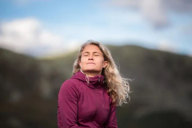 Kvinna med slutna ögon i rosa tröja mot fjällbakgrund